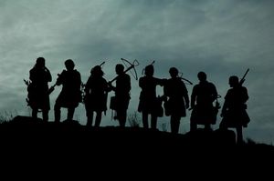Silhouette of a group of eight medieval style soldiers with crossbows against a cloudy sky.