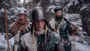 Three medieval style soldiers in green and white clothing standing in a snow covered forest.